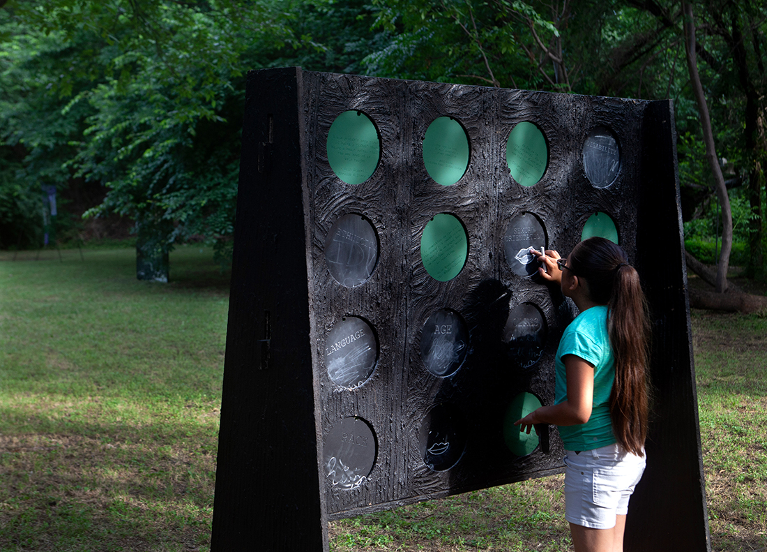 Sculpture in a field, a flat board with sixteen holes, supported by two legs