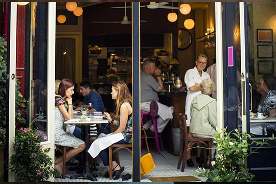 Two young women sit facing each other by an open door eating