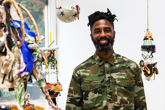 man in camouflage shirt surrounded by hanging sculptures