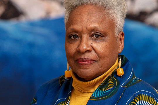 A woman in blue jacket, yellow shirt in front of blue background