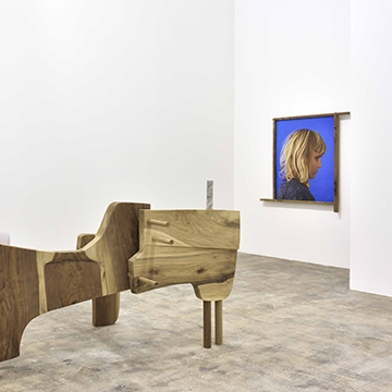 Image of an installation of an abstract wooden sculpture with curving lines and a photo of a young blonde girl in profile