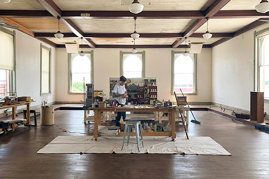 man stands amid his art supplies in a corsicana art studio